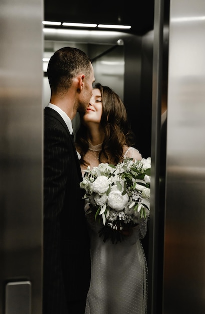 Os recém-casados se beijam quando as portas do elevador se fecham. o noivo e a noiva estão felizes. casal de noivos pega o elevador para o ciremônio de casamento