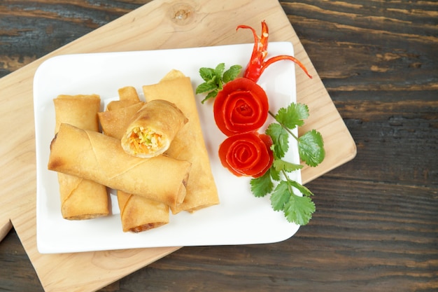 Foto os rolos de mola chineses fritados serviram com molho de pimentão e tomates cor-de-rosa decorados com verde com folhas na madeira, espaço. comida asiática de conceito