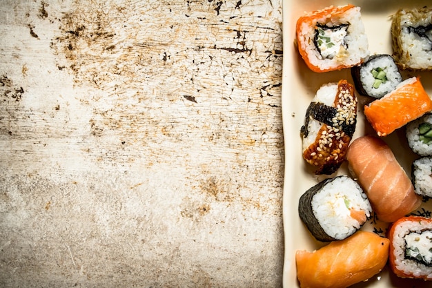 Os rolos e sushi, frutos do mar no prato. Sobre fundo rústico.