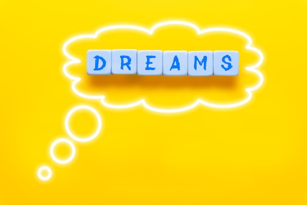 Os sonhos de palavra escritos em cubos e emoldurados com balão de pensamento em fundo amarelo. Aspirações futuras sobre o conceito de vida, carreira ou negócio.