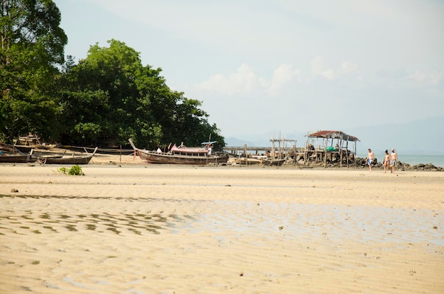 Os tailandeses param o barco de pesca de madeira para reparo e viajantes estrangeiros andando na praia no oceano de andaman em Koh Yao Noi em 7 de junho de 2016 em Phang Nga Tailândia