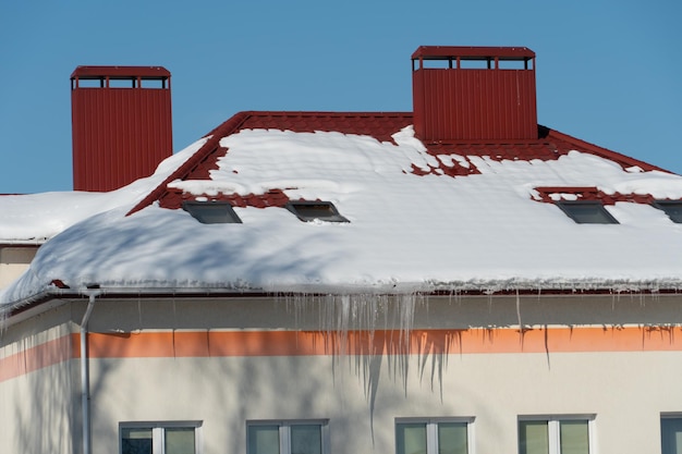 Os telhados dos edifícios estão cobertos de neve e gelo após uma grande queda de neve Enormes pingentes de gelo pendem das fachadas dos edifícios A queda de pingentes traz um perigo para a vida das pessoas