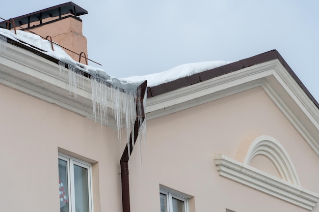 Os telhados dos edifícios estão cobertos de neve e gelo após uma grande queda de neve Enormes pingentes de gelo pendem das fachadas dos edifícios A queda de pingentes traz um perigo para a vida das pessoas