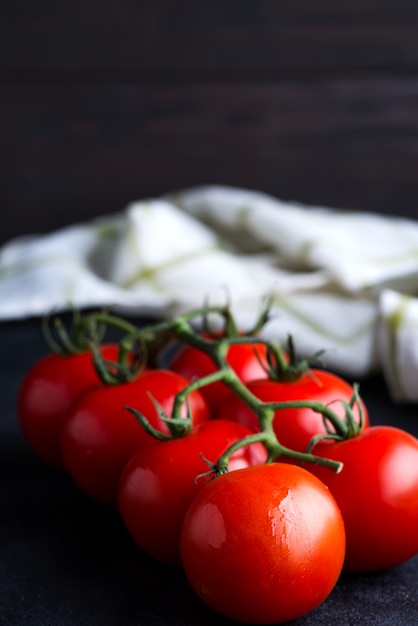 Os tomates orgânicos maduros frescos ramificam em um fundo escuro com toalha de matéria têxtil.