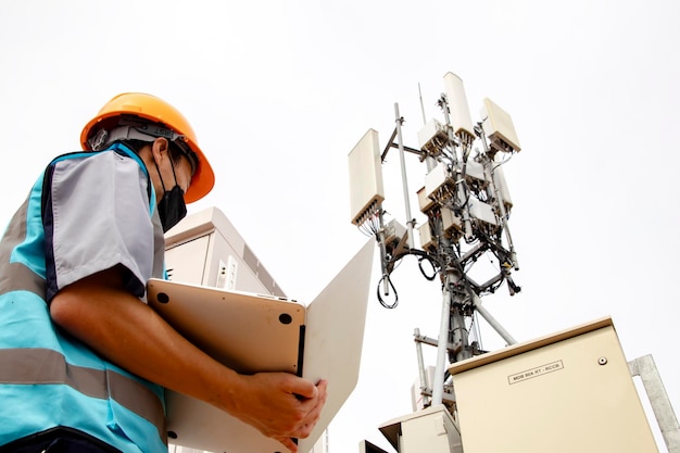 Os trabalhadores asiáticos da eletrônica do homem mascarado controlam a rede 5G dos sistemas de TI da estação de telecomunicações.