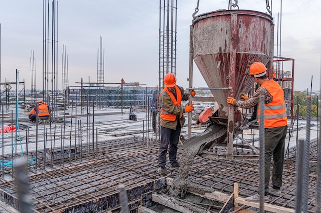 Os trabalhadores em um telhado de infraestrutura de construção com máquinas e ferramentas Despejando concreto em um molde