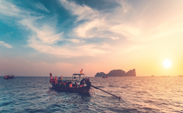 Os tradicionais barcos de pesca com os turistas no oceano próximo às exóticas Ilhas Phi Phi, no Reino da Tailândia. Fundo do sol colorido de tirar o fôlego. Beleza da natureza selvagem.