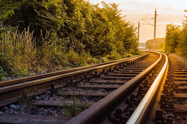 Os trilhos de trem se distanciam contra o pano de fundo do pôr do sol.