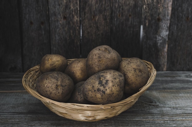 Os tubérculos de batatas em uma cesta de vime em um fundo de madeira