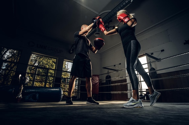 Foto en el oscuro gimnasio en el ring, la entrenadora experimentada y la joven tienen una pelea de kick boxing.