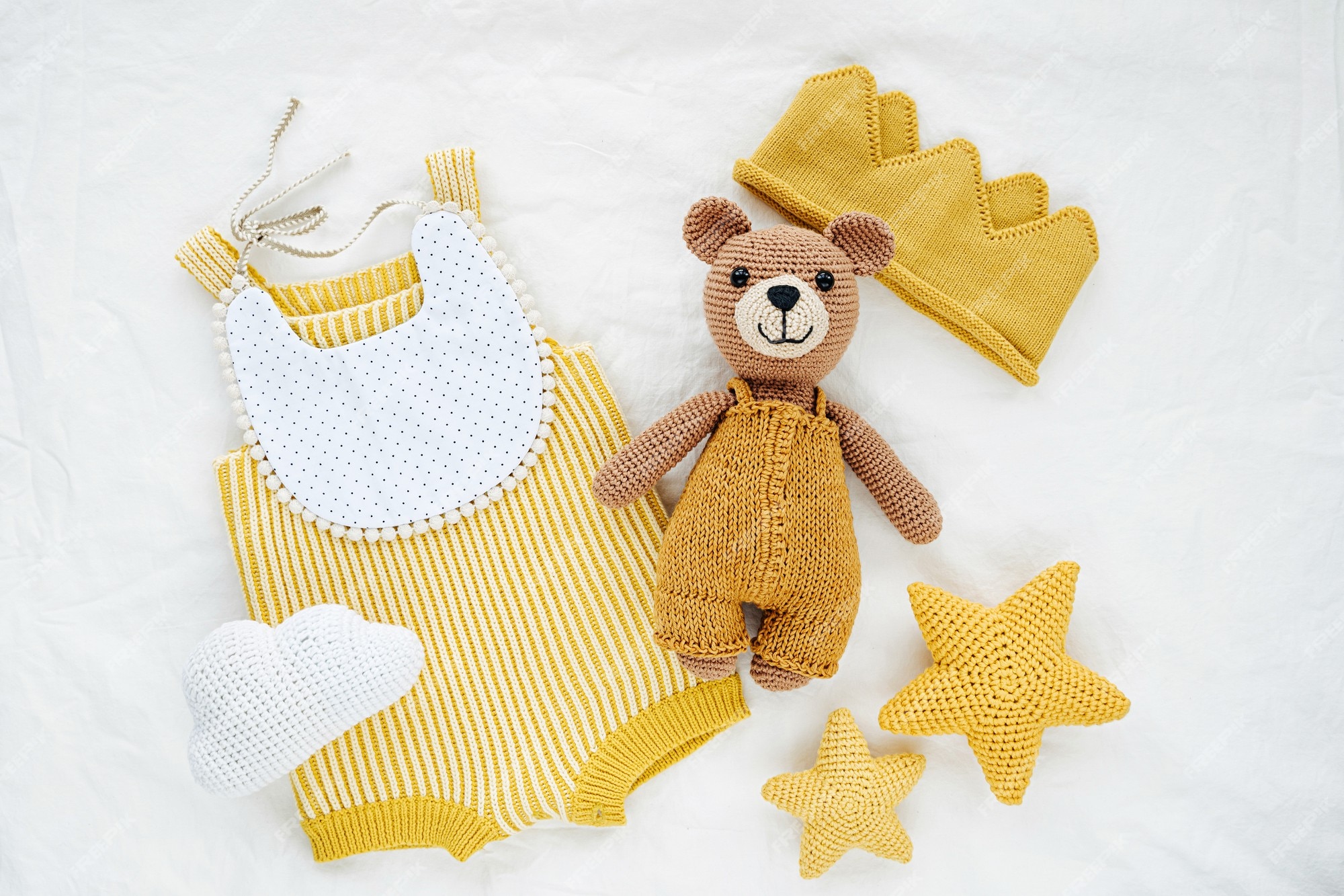 Oso juguete de punto, mameluco amarillo y estrellas de juguete para recién nacido en cama blanca. ropa accesorios para bebés de género neutro. endecha plana, vista superior Foto Premium