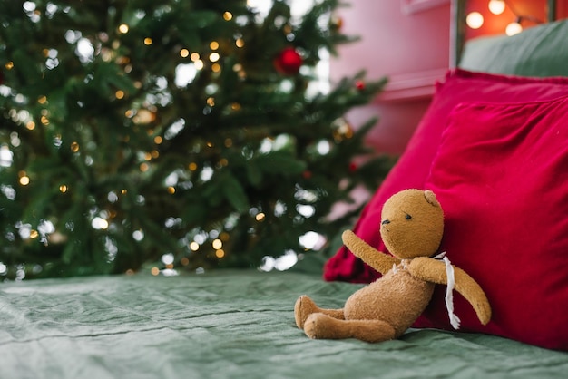 Oso de juguete vintage en la cama cerca de las almohadas en el fondo de las luces de Navidad