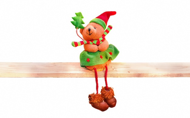 Oso de Navidad de peluche con un árbol de Navidad verde sentado en un estante de madera. El objeto está aislado en un fondo blanco.