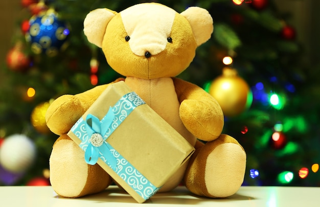 Oso de peluche y caja de regalo sobre fondo de árbol de Navidad