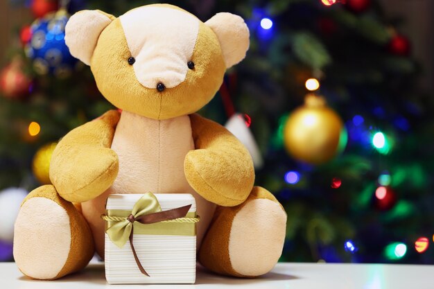 Oso de peluche y caja de regalo sobre fondo de árbol de Navidad