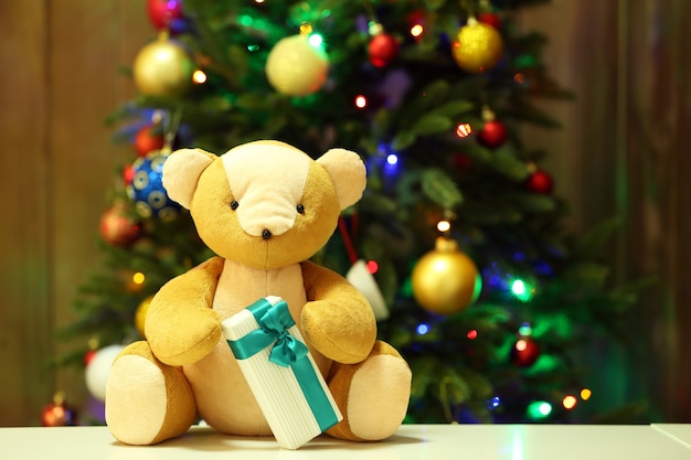 Oso de peluche y caja de regalo sobre fondo de árbol de Navidad