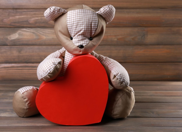 Oso de peluche con corazón rojo sobre fondo de madera