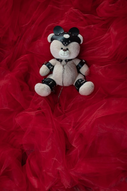 Un oso de peluche de juguete vestido con cinturones de cuero y una máscara, un accesorio para juegos BDSM