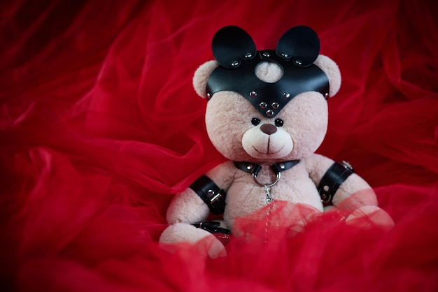 Un oso de peluche de juguete vestido con cinturones de cuero y una máscara, un accesorio para juegos BDSM