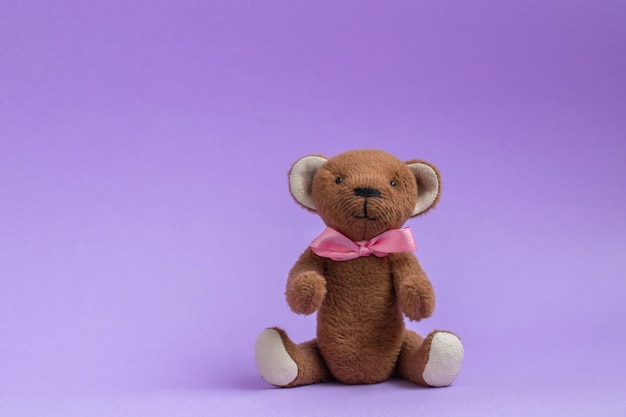 Foto oso de peluche sentado sobre fondo púrpura juguete de oso de peluche con lazo rosa