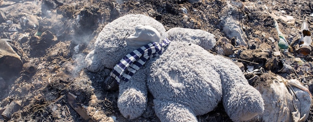 Un oso de peluche yace tirado en medio de un vertedero de basura humeante