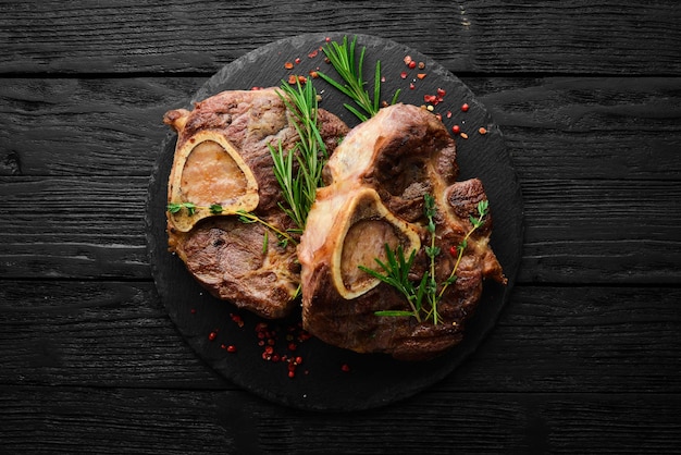 Osso buco pierna de ternera cocida con especias y romero Carne a la barbacoa Vista superior Vista superior plana sobre mesa de corte de piedra negra