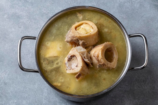 Osso cozido e caldo. Caldo de osso de carne caseiro é cozido em uma panela. Os ossos contêm colágeno, que fornece ao corpo aminoácidos, que são os blocos de construção das proteínas.