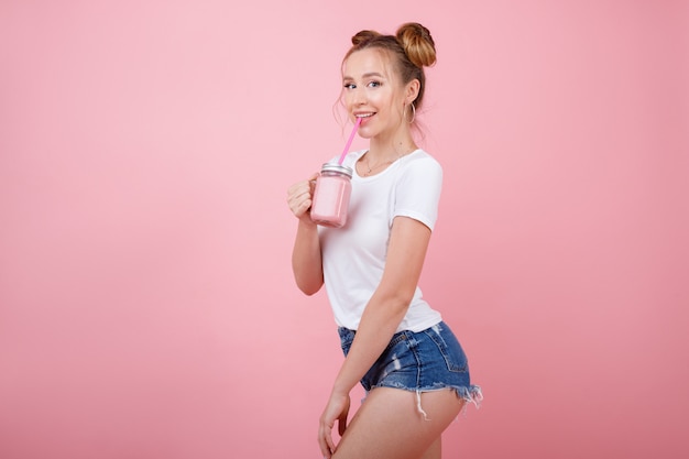 Ostentando uma garota saudável com um copo de smoothies em um espaço rosa. Alimentação saudável