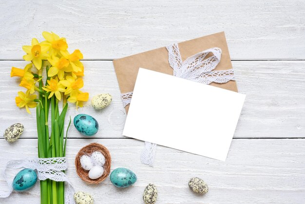 Foto oster-grüßkarte mit gelben narzissblumen und farbenfrohen oster-eiern auf weißem holz