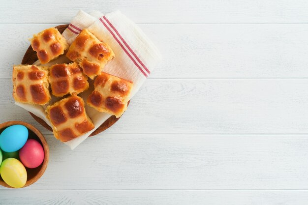 Oster-Hot-Cross-Brötchen mit farbigen Eiern Oster-Lebkuchen-Kaninchen und Kekse auf weißem Plankenholz-alten Tischhintergrund Frühlingsferien-Backkonzept Ostern-Tischeinstellung Draufsicht Mock-up