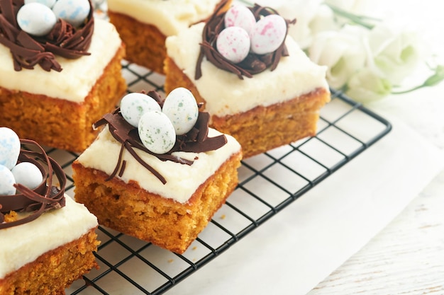 Oster-Karottenkuchen mit Schokoladennest und Schokoladen-Eiern, Blüten von Kirschen- oder Apfelblumen auf rustikalen hellen Holz-Hintergründen Osterfeiern, traditionelles Osteressen