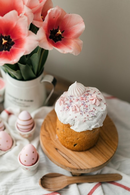 Oster-Panettone und gefärbte Ostereier. Ostersymbole. Rosa Tulpen im Metallkrug auf Holztisch