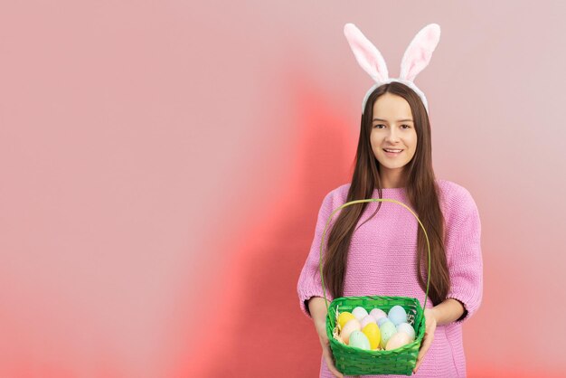 Osterbanner Fröhliches Mädchen in den Hasenohren mit einem Korb dekorierter Eier lächelnd auf rosa Hintergrund im Studio mit Kopierraum