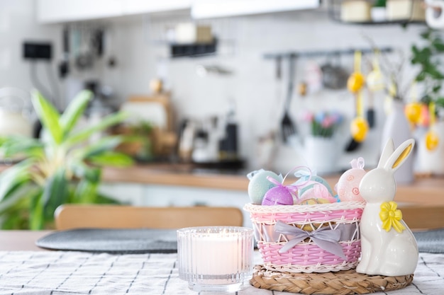 Osterdekoration aus bunten Eiern in einem Korb und einem Kaninchen auf dem Küchentisch im rustikalen Stil Festliches Interieur eines Landhauses