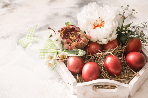 Osterdekoration mit einem Korb und roten Eiern mit Blumen