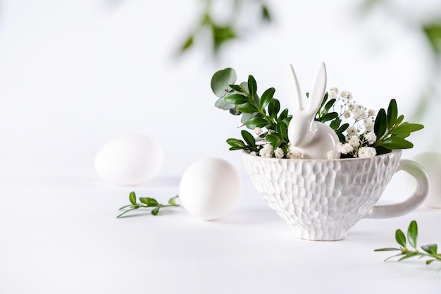 Osterei und Frühlingsblumen mit Häschen in Teetasse auf weißem Hintergrund Kreatives Osterferienkonzept Minimale Grußkarte mit Kopierplatz für Text