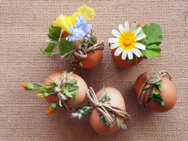 Ostereier, die mit natürlichen Blumen auf einem Hintergrund aus Sackleinen dekoriert sind