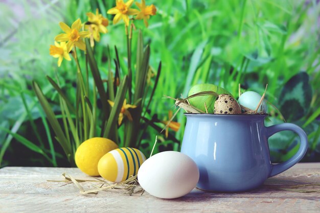 Ostereier eine Tasse mit Osterschmuck und eine Blume auf einem Holztisch