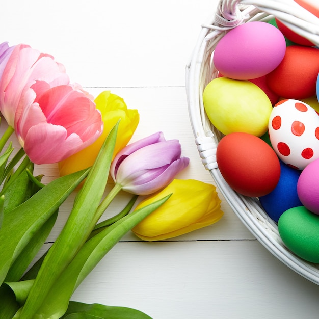 Ostereier im Korb und im Frühling bunte Blumen auf weißem Holztisch mit Kopienraum