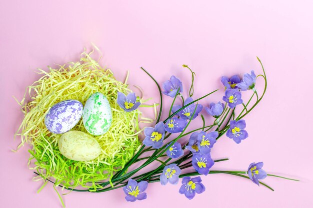 Ostereier im Nest und Frühlingsblumen auf rosafarbenem Hintergrund Frohes Osterkonzept