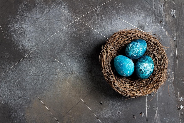 Foto ostereier im nest von hand in blauer farbe auf dunklem hintergrund bemalt