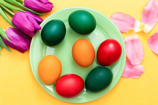 Ostereier mit Tulpen auf einem grünen Teller auf einem gelben