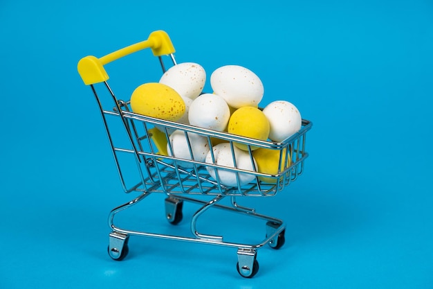 Ostereier mit weißen und gelben Wachteln in einem Einkaufswagen auf blauem Hintergrund