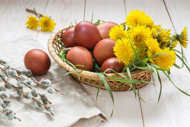 Ostereier und ein Blumenstrauß Löwenzahn auf einem weißen Tisch.