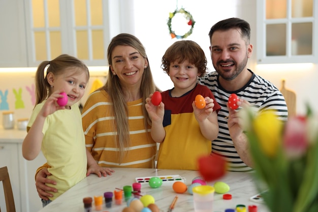 Osterfeier Porträt einer glücklichen Familie mit bemalten Eiern an einem weißen Marmortisch in der Küche