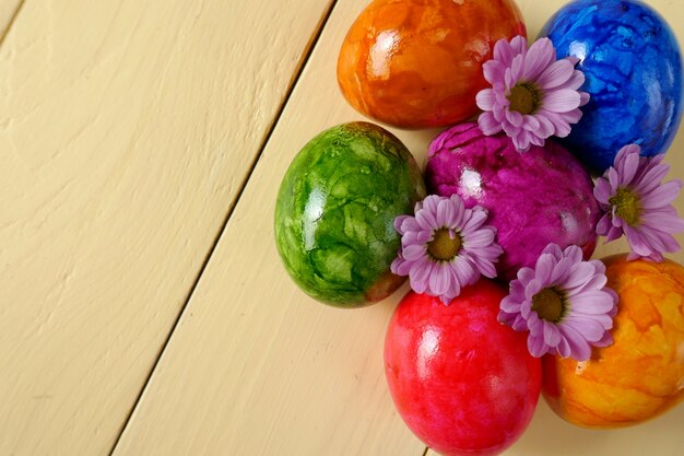 Osterferien. Ostereier mit lila Chrysanthemenblumen auf gelber Brettoberfläche