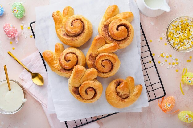 Osterfrühstück Holliday-Konzept Osterbrötchen mit Zimtbrötchen aus Hefeteig mit orangefarbener Glasur Osterschmuck farbige Eier auf rosa Frühlingshintergrund Osterholliday-Karte