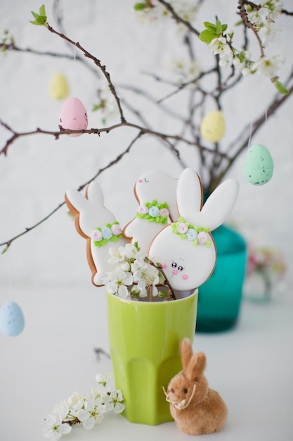 Osterglasierte Kekse in grüner Vase in der Nähe von Osterbaum mit bunten Eiern