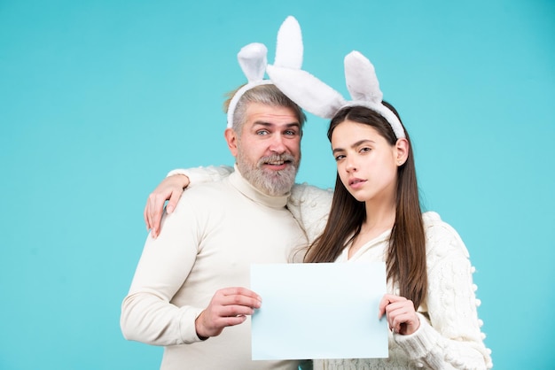 Osterhasenpaar mit Papier für Textkopierraum Paar gekleidet in Kostüm Osterhase auf blauer Ba...