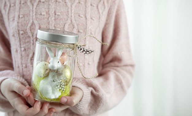 Osterhintergrund mit einem Glas mit festlichem Dekor in Kinderhänden